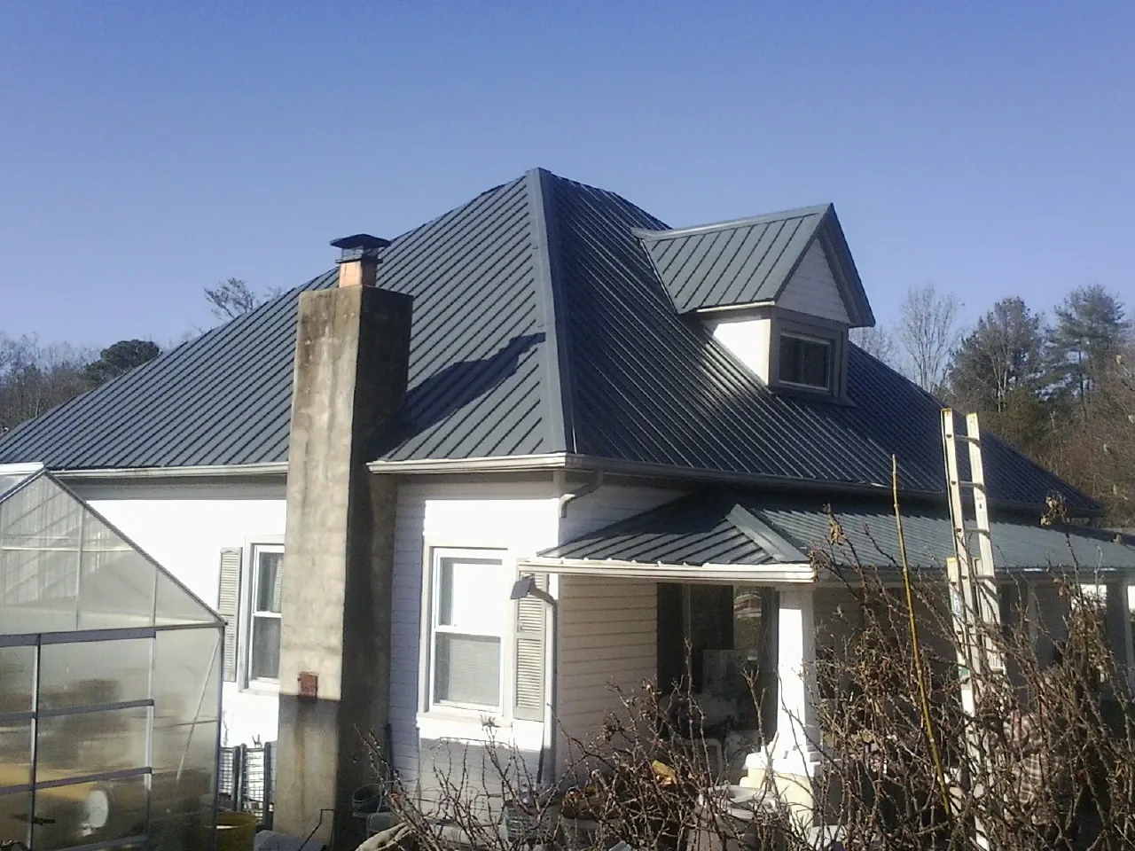 Dark blue standing seam metal roof on a white farmhouse with dormer — Slate & Tile Roof Repair by Roofing Brothers in North Wilkesboro