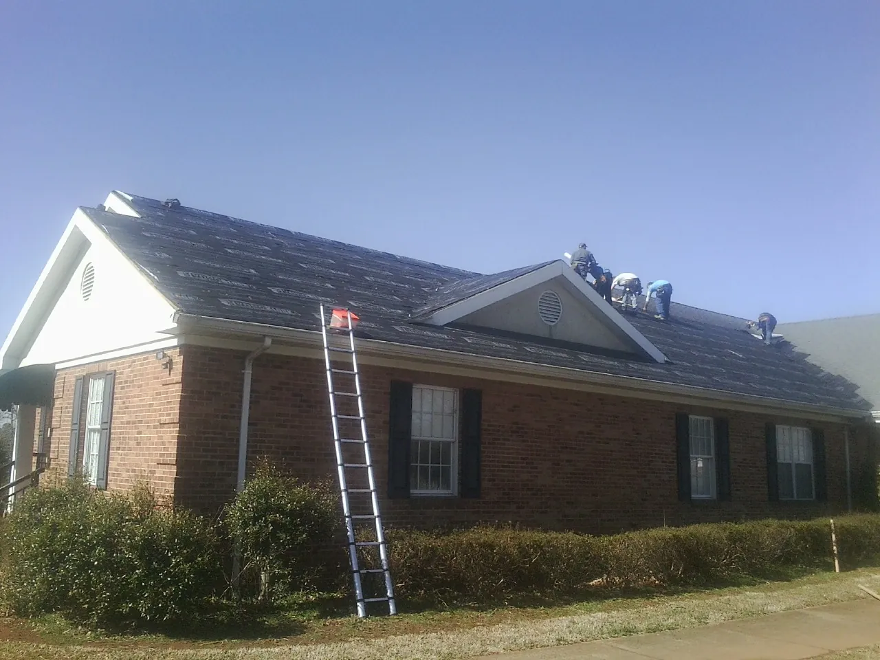 Crew tearing shingles off a brick ranch roof with a ladder set — Emergency Roof Repair work by our crew in North Wilkesboro