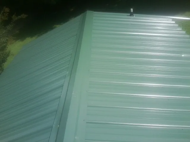 New green metal panels meeting at the ridge of a roof — Flat Roof Repair work by our crew in North Wilkesboro