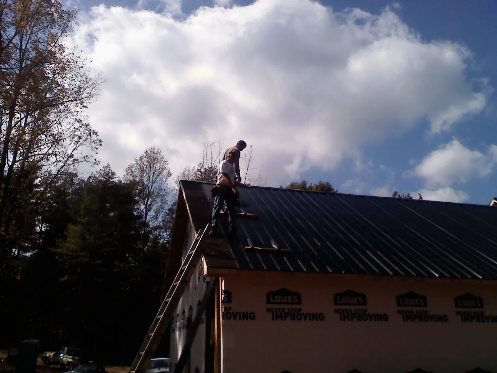 Roofer fastening dark metal panels high against a cloudy sky, from a Roof Inspection job in North Wilkesboro