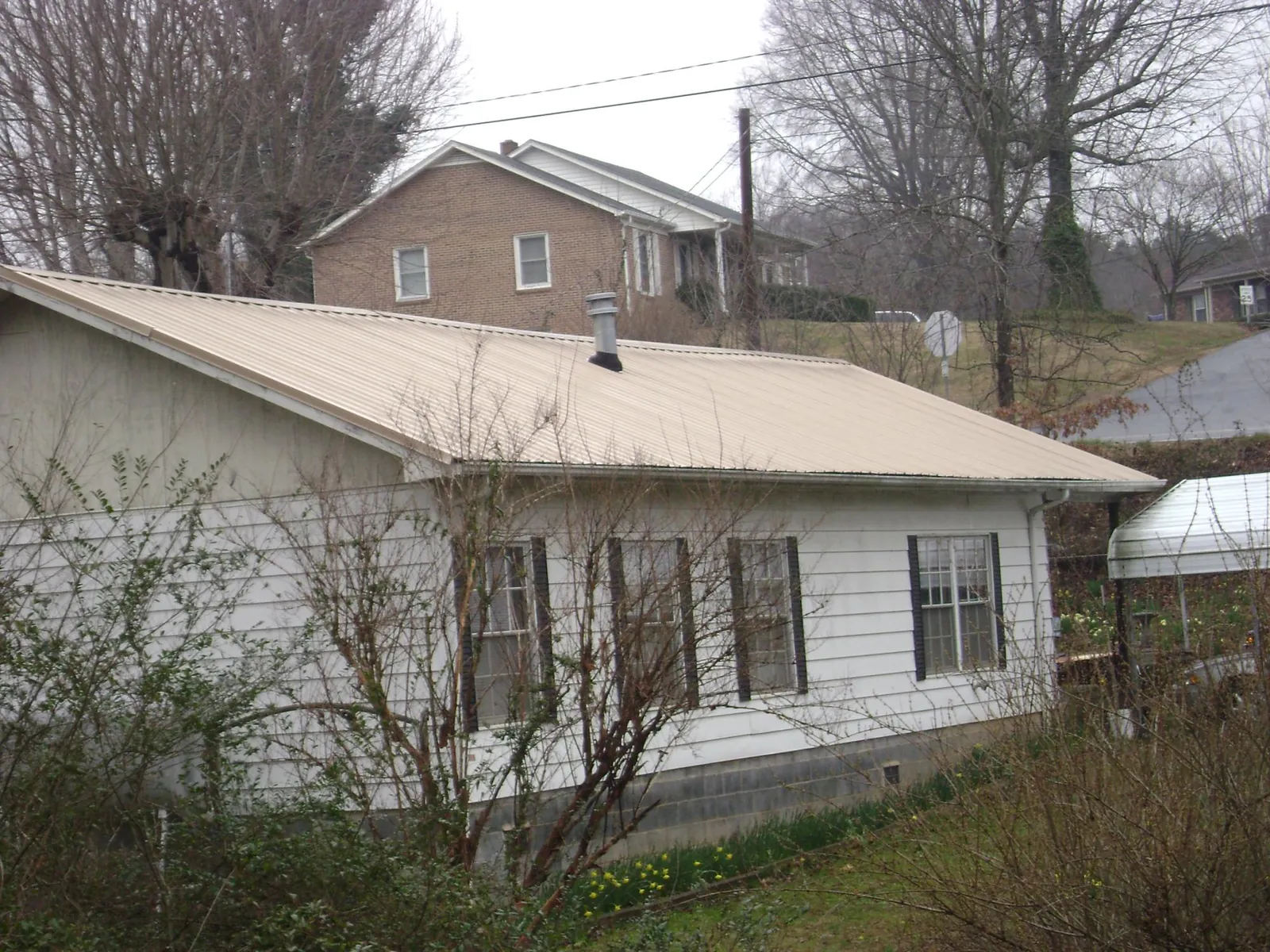 Tan metal roof on a white sided house set into a hillside — Commercial Roofing by Roofing Brothers in North Wilkesboro